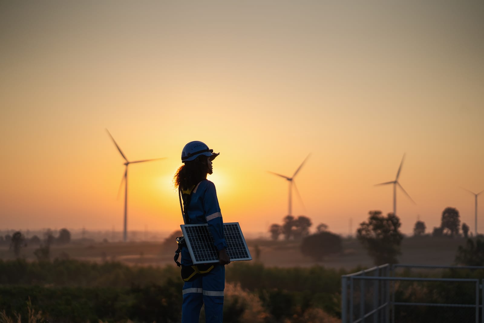 Fachkraft mit Solarmodul vor Windenergieanlagen